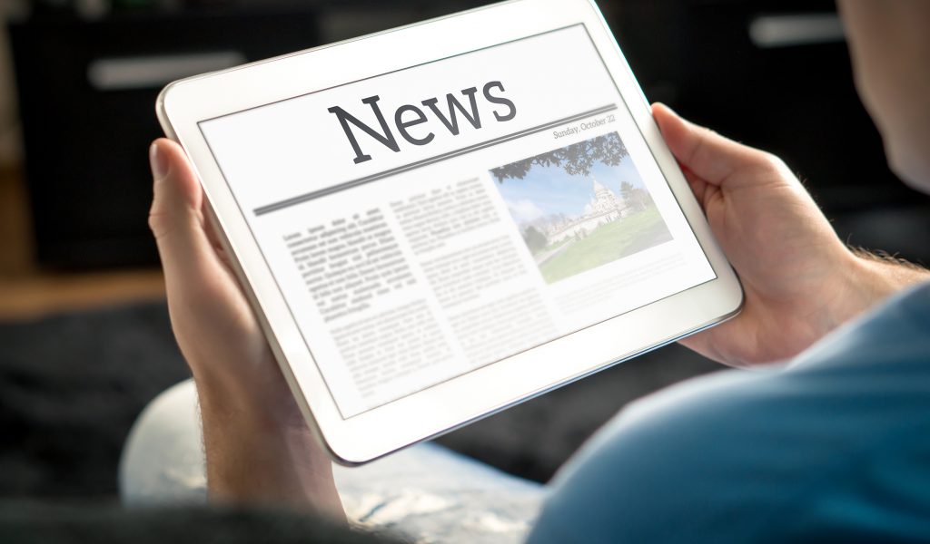 Man reading the news on tablet at home. Imaginary online and mob Man reading the news on tablet at home. Imaginary online and mobile news website, application or portal on modern touch screen display. Holding smart device in hand.